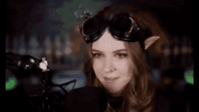 a woman with elf ears and goggles is standing in front of a microphone .