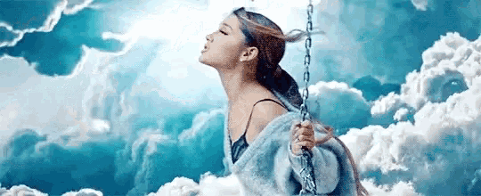 ariana grande is sitting on a swing in the clouds with her eyes closed .