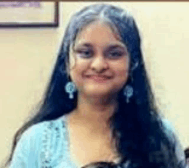 a woman with long hair and earrings is smiling for the camera in a room .