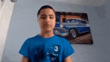a young boy in a blue shirt is standing in front of a painting of a blue car on the wall .