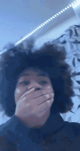 a person with an afro covering their mouth with their hands