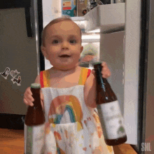 a baby in a rainbow dress is holding two bottles of beer in front of an open refrigerator .