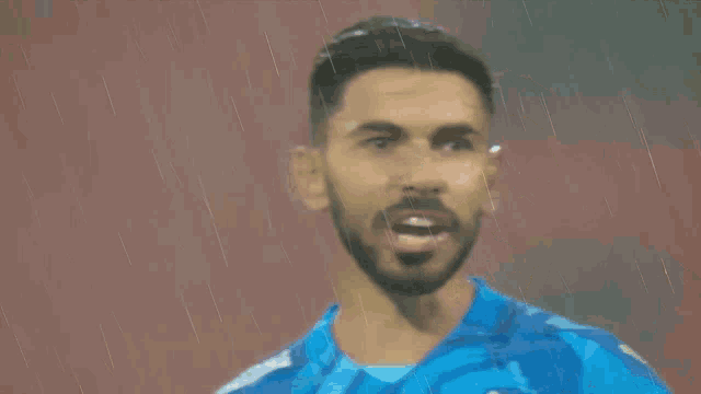a man in a blue shirt stands in the rain with his mouth open