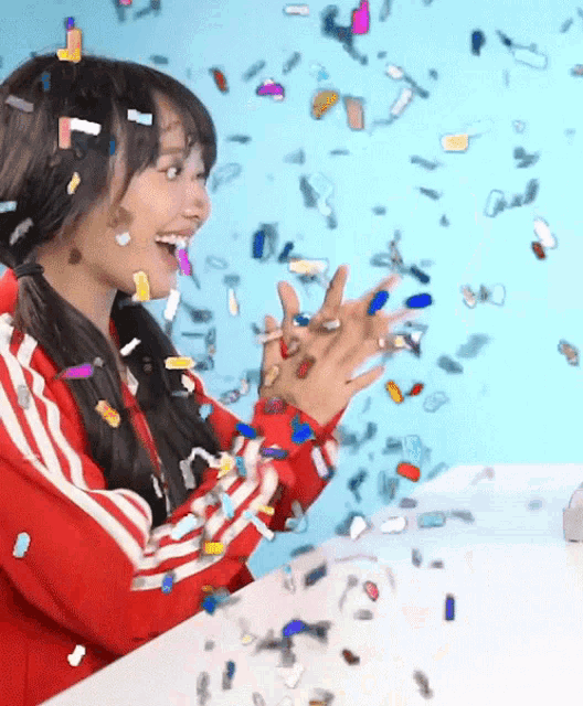 a woman in a red jacket is surrounded by confetti and smiling