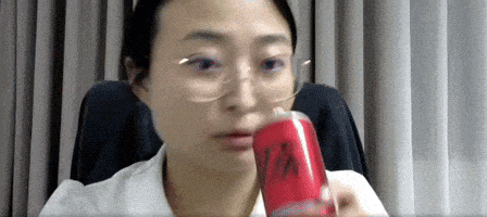 a woman wearing glasses is holding a can of soda in her hand .