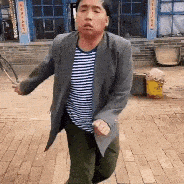 a man wearing a striped shirt and a grey jacket is jumping rope