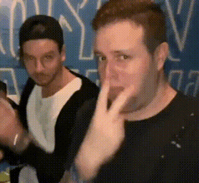 two men are sitting at a table and one of them is making a peace sign .