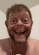 a shirtless man with a beard is smiling and wearing a gold chain