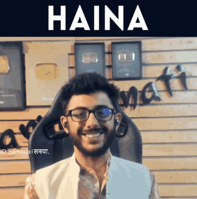 a man wearing glasses is smiling in front of a wall that says haina