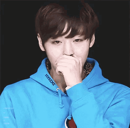 a young man wearing a blue supreme hoodie is covering his mouth .