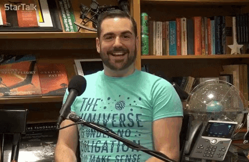 a man wearing a blue shirt that says the universe is smiling in front of a microphone
