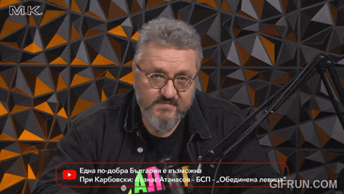 a man with glasses and a beard is sitting in front of a microphone with mk written on the top