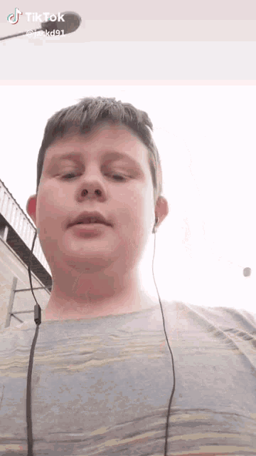 a young boy wearing headphones and a grey shirt is looking at the camera with a tik tok watermark