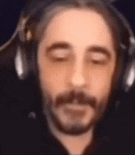 a man with a beard is wearing headphones and looking down .