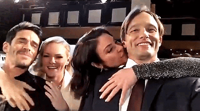 a group of people are posing for a picture and one of them is kissing another man on the cheek