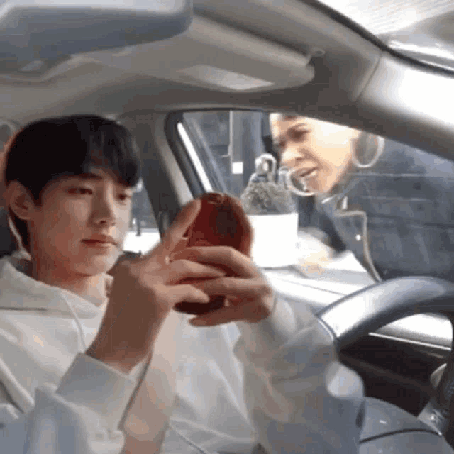 a man is sitting in a car looking at his phone while a woman looks on .