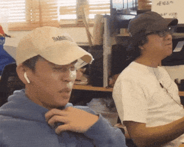 a man wearing a balenciaga hat sits next to another man wearing headphones
