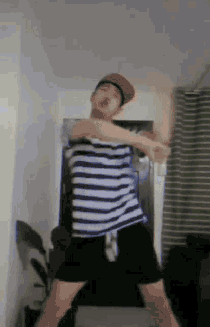 a man wearing a striped shirt and a hat is dancing in a room
