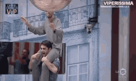 a man is carrying another man on his shoulders in front of a building on a tv show .