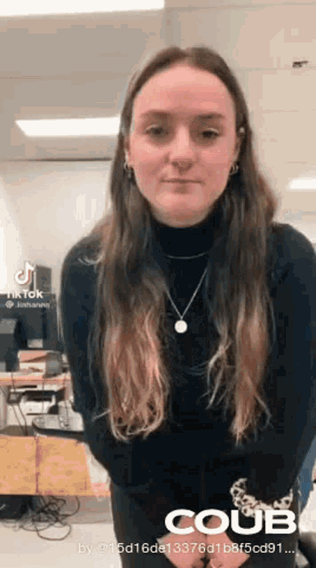 a woman wearing a black turtleneck and a necklace is standing in front of a desk .