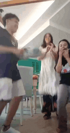 a group of people are dancing in a room with a table and chairs