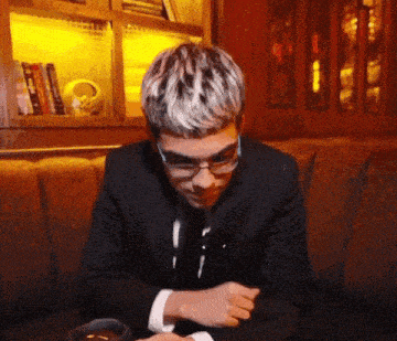 a man wearing glasses and a suit is sitting on a couch