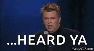 a man is standing in front of a microphone holding a glass of wine and says `` heard ya '' .