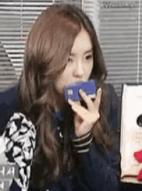 a woman is sitting on a couch holding a cell phone to her mouth .