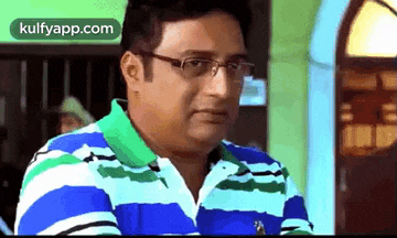 a man wearing glasses and a striped shirt is sitting in front of a window .