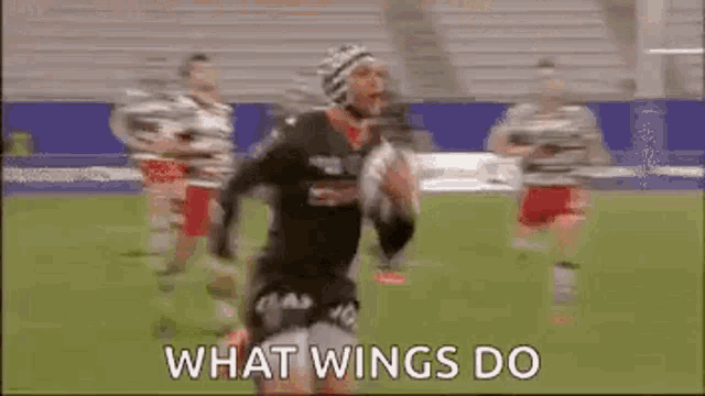 a man is running with a rugby ball on a field and the words `` what wings do '' are written on the screen .