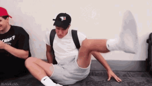 a man is sitting on the floor with his leg up while another man watches .