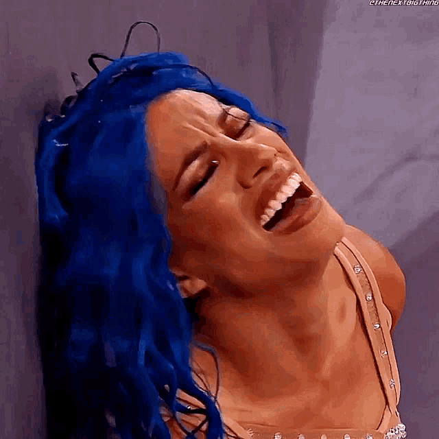 a woman with blue hair is leaning against a wall and laughing .