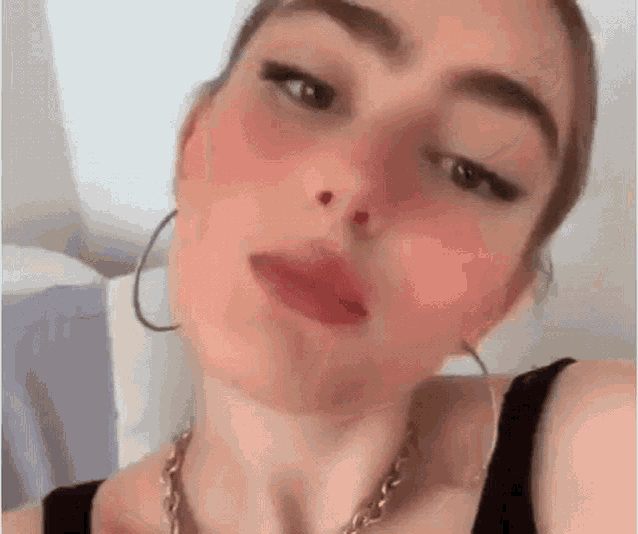 a woman wearing hoop earrings and a necklace is taking a picture of herself .