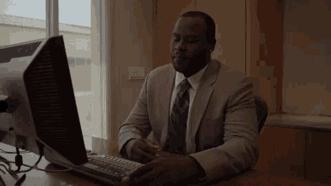 a man in a suit and tie is typing on a laptop computer
