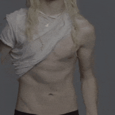 a man with long blonde hair is taking off his white shirt