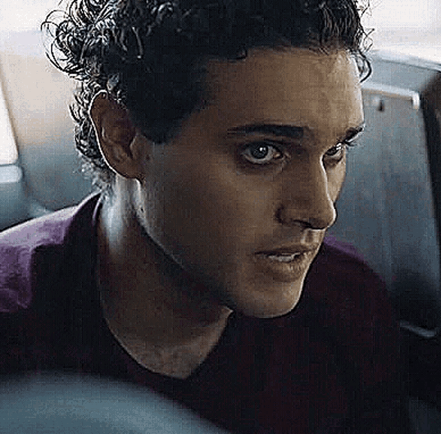 a man with curly hair is sitting in the back seat of a car looking at something .