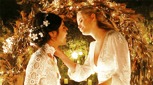 two women in wedding dresses are kissing in front of a wreath of lights