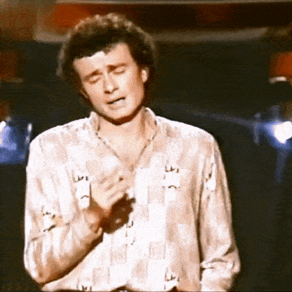 a man in a checkered shirt is singing into a microphone .