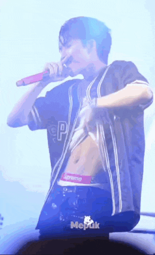 a man in a supreme shirt is singing into a microphone on stage .