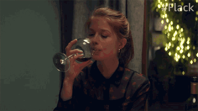 a woman drinking from a wine glass with the hashtag #flack visible