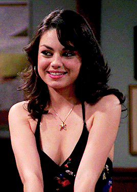 a woman wearing a black top and a necklace smiles