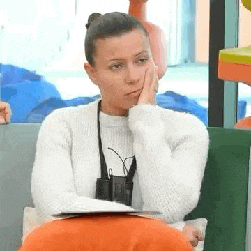 a woman in a white sweater is sitting on a couch with her hand to her face .