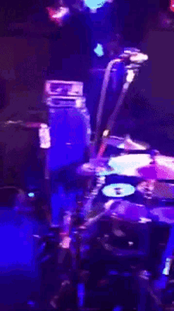 a man playing drums in a dark room with purple lights