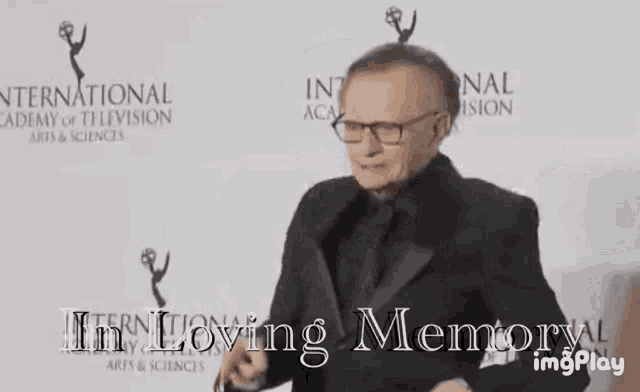 a man in a tuxedo and glasses is standing in front of a sign that says i 'm loving memory