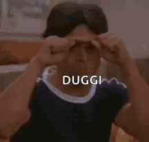 a man is making a funny face with his fists in the air and the word duggi is written on his face .