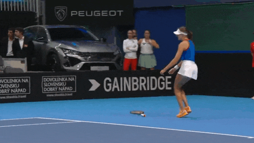 a woman holding a tennis racquet on a tennis court in front of a gainbridge sign