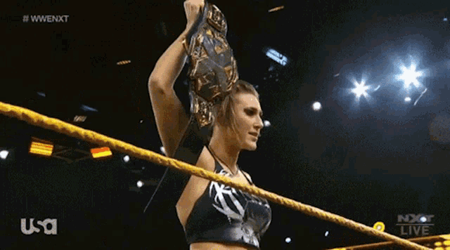 a woman in a wrestling ring holding a championship belt with the usa logo on the bottom right