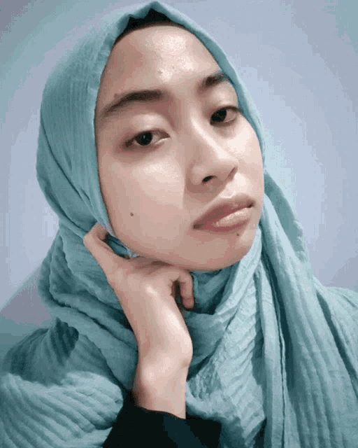 a woman wearing a light blue hijab holds her hand to her face