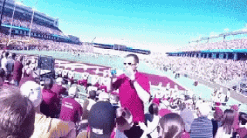 a man is holding a child in his arms in a stadium while a crowd watches .