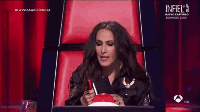 a woman is sitting in a red chair reading a book and the words infiel are on the screen behind her